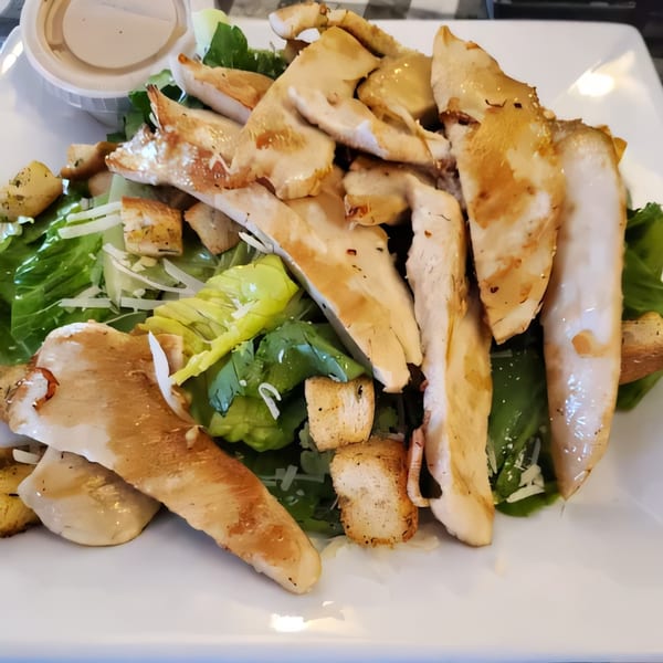 A Caesar salad with grilled chicken, croutons, and parmesan cheese, served with dressing on the side.