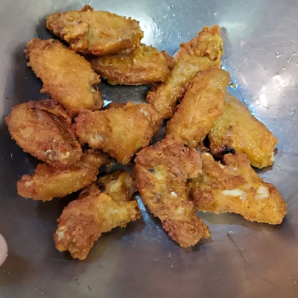 A close-up of golden-brown fried chicken wings in a metal bowl, ready to be served.