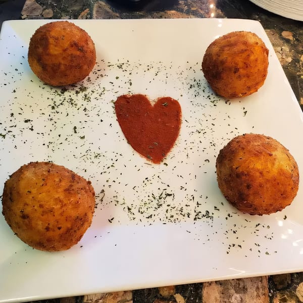 Four golden-brown arancini balls on a white plate, with a heart shape made of spice.