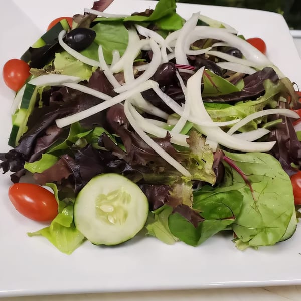 Fresh Italian salad with mixed greens, cherry tomatoes, cucumbers, black olives, and sliced onions.