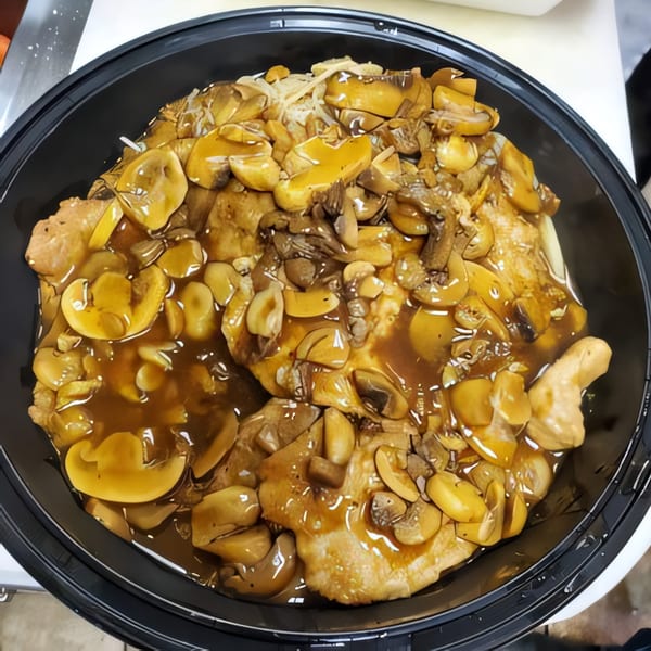 Chicken and mushrooms in a rich brown sauce, served in a black takeout container.