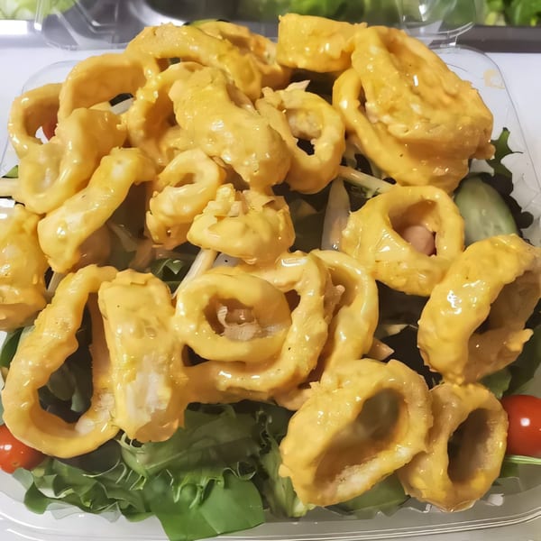 Fried calamari rings with a creamy sauce, served over a bed of green lettuce and cherry tomatoes.